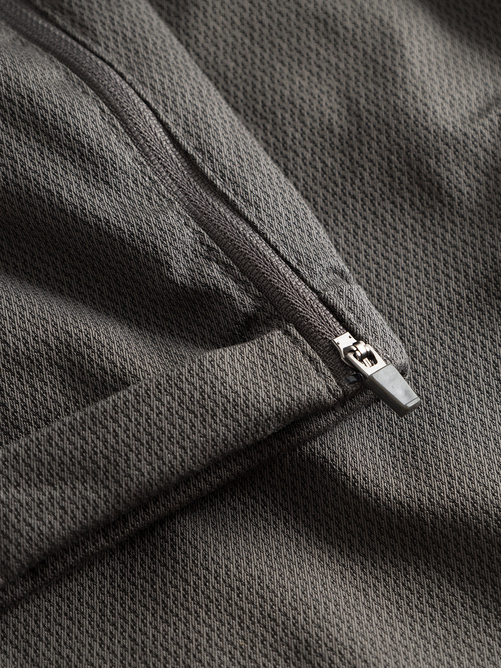 Close-up of the Pisa K3280 Dale Pants - Grey by GABBA: dark gray, high-stretch cotton-blend fabric with a subtle diamond pattern and partially open metallic zipper, offering a textured surface and stylishly tapered fit for modern city wear.