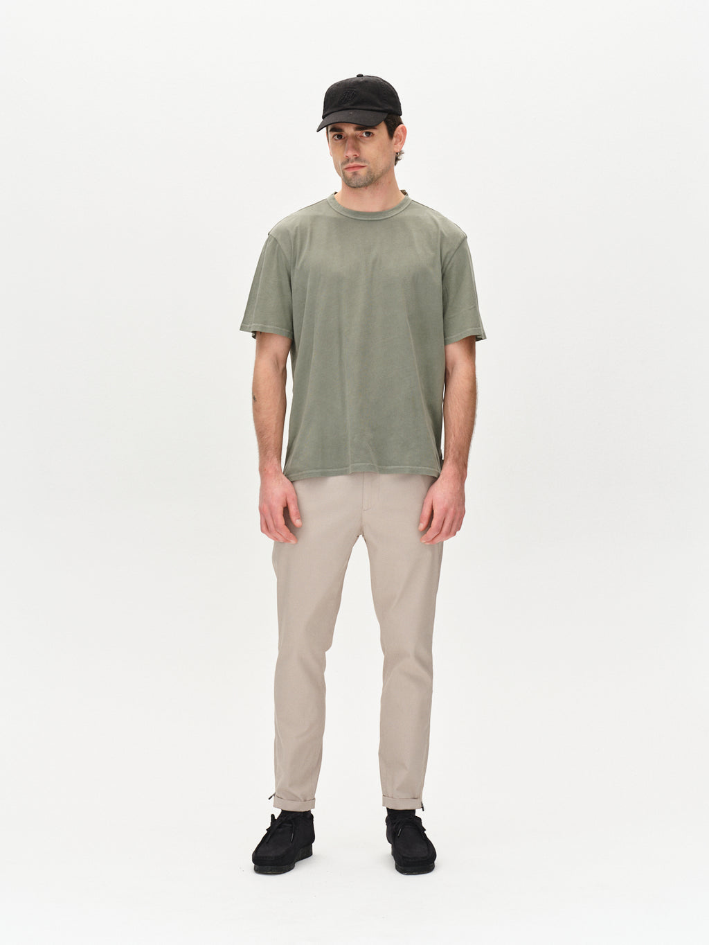 A man in a dark cap, green shirt, Gabba Pisa K3280 Dale Pants in Grey Paloma, and black shoes stands against a white background with his arms at his sides.