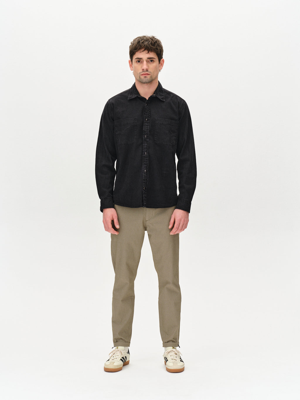 A man wearing a black button-up and Gabbas Pisa K3280 Dale Pants in olive green, made from a high-stretch cotton-blend, stands against a plain white background. He wears white sneakers, has short hair, and shows a neutral expression.