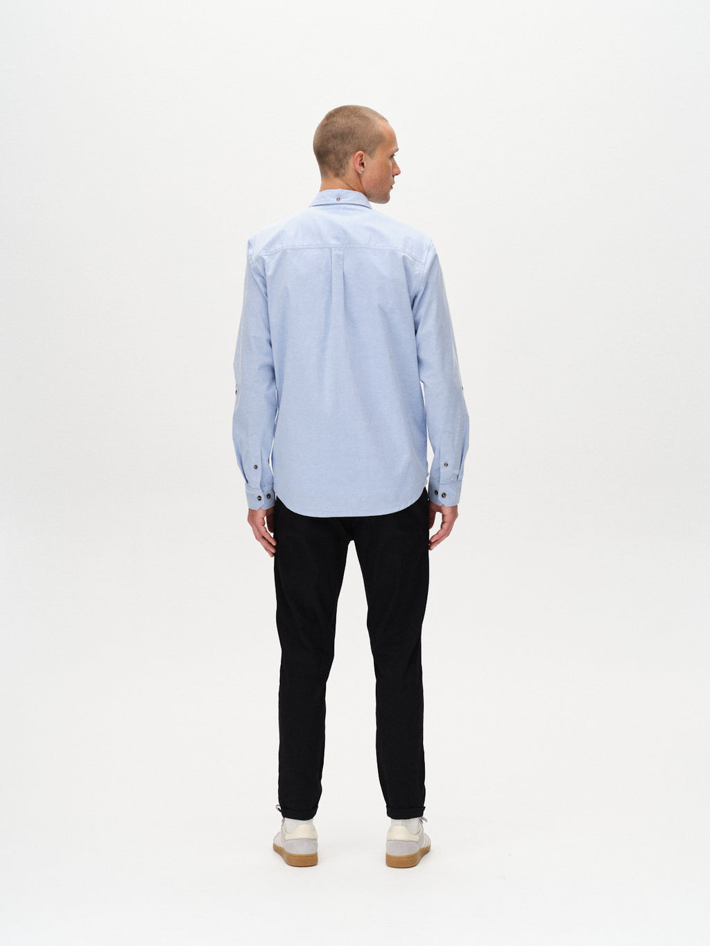 A person stands facing away from the camera, wearing a light blue long-sleeve shirt, Gabba Pisa K3280 Dale Pants in black with a tapered fit, and white shoes, set against a plain white background.