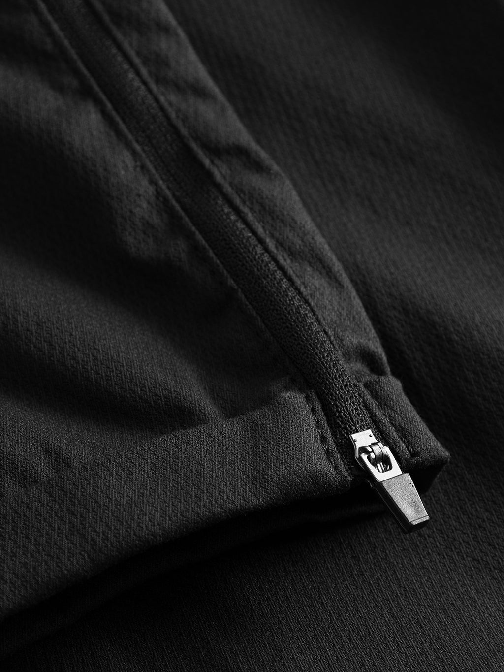 A close-up of the Pisa K3280 Dale Pants - Black by Gabba shows a sleek design with high-stretch, textured cotton-blend fabric. The partially open diagonal zipper and metallic pull create a stylish contrast against the dark background, epitomizing modern city fashion.