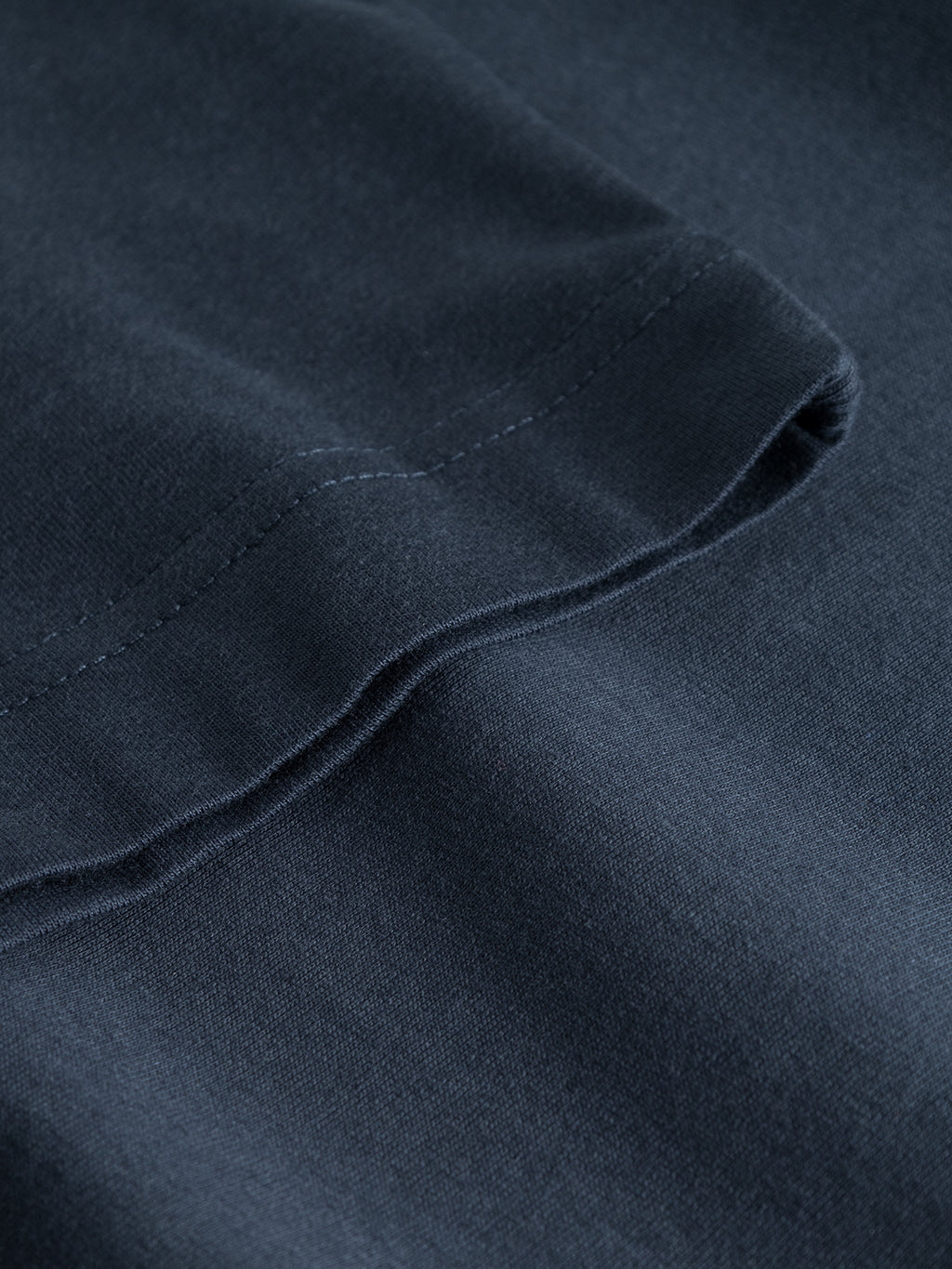 Close-up of the Dune SS GOTS Tee - Total Eclipse by Gabba, crafted in navy blue from GOTS-certified organic cotton. Visible stitching along the edge highlights its texture and smooth surface.