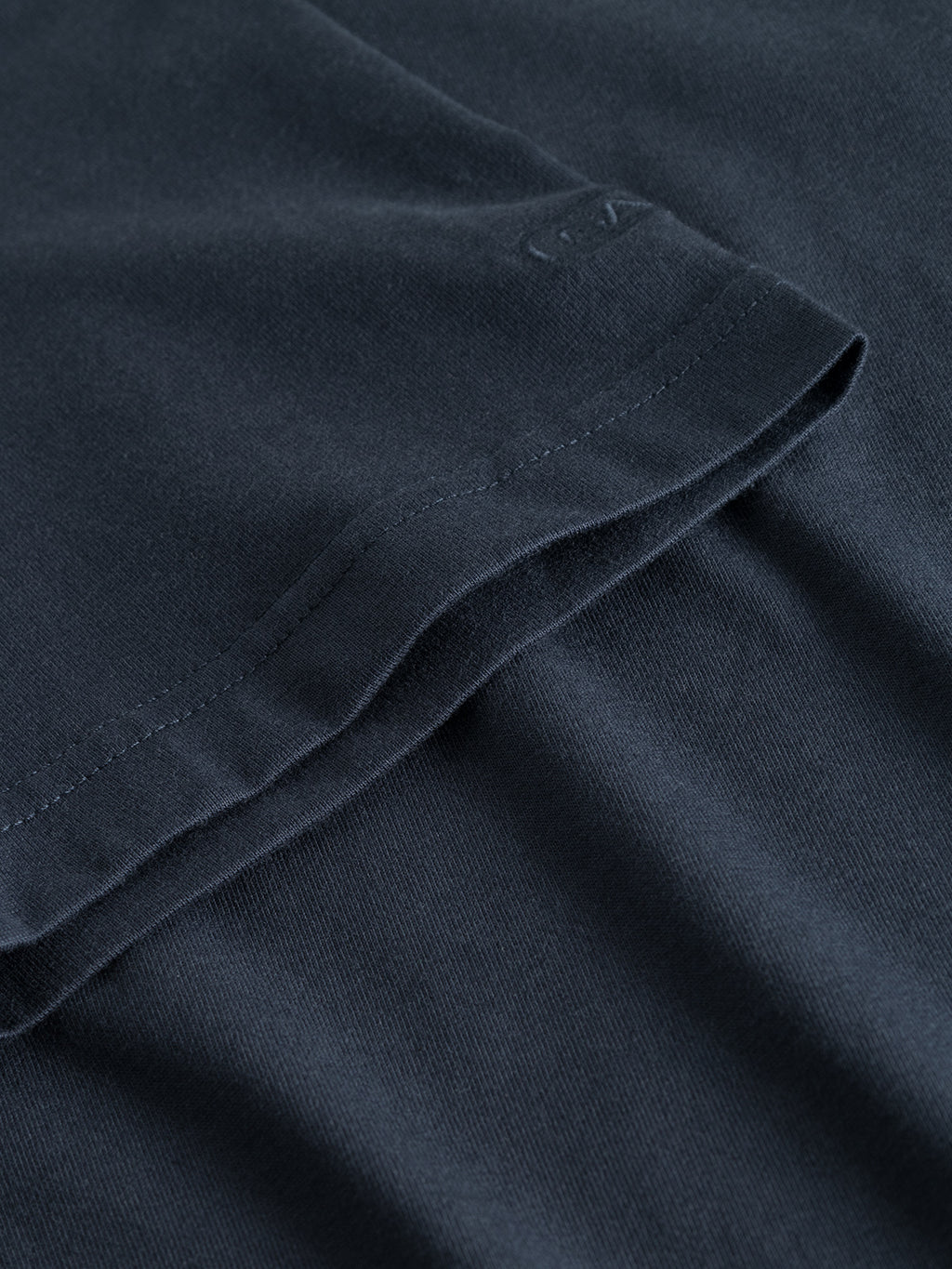 A close-up of the Dune SS GOTS Tee - Total Eclipse by Gabba shows black folded fabric made from organic cotton, highlighting its detailed stitching and texture.