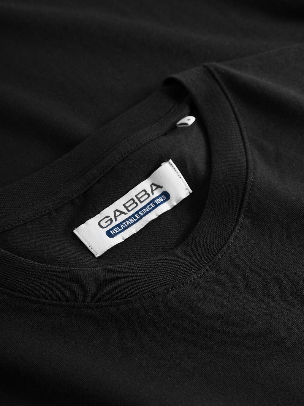 Close-up of a Dune SS GOTS Tee in black, featuring the Gabba label sewn inside the collar, reading RELIABLE SINCE 1983. Made from organic cotton, the fabric is smooth with neat stitching.