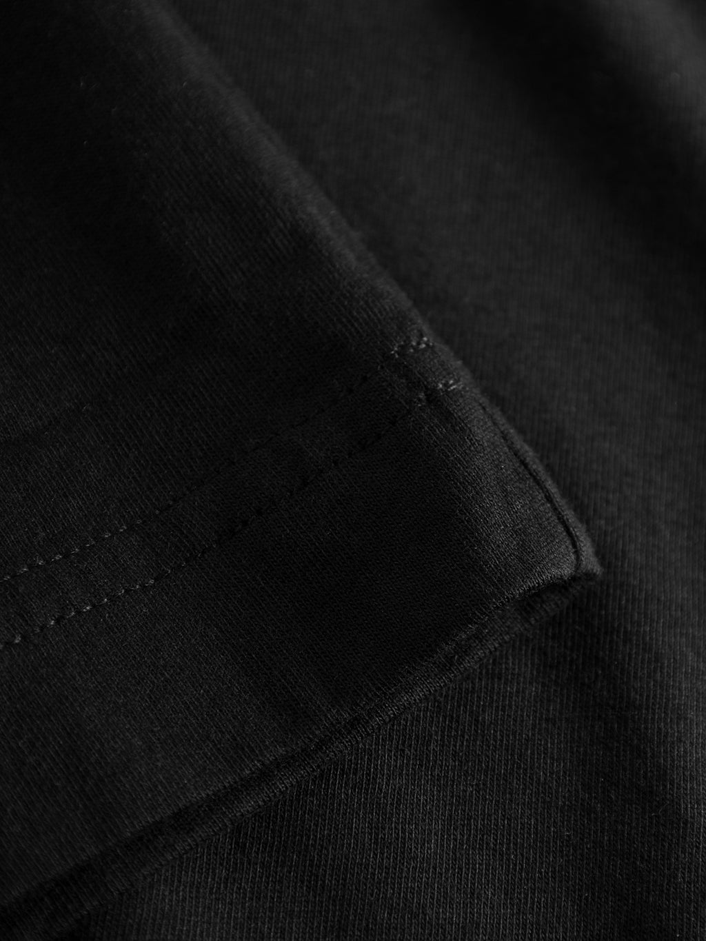 Close-up of the Dune SS GOTS Tee - Black by Gabba, highlighting detailed stitching on a hem. The smooth, slightly glossy texture made from organic cotton showcases quality craftsmanship typical of a classic fit t-shirt.