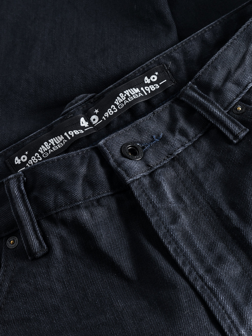 Close-up of Gabbas Carl Selvedge 40th Anniversary - Blue Black Denim pants, highlighting the waistband with size label 40 and 1983. The buttoned, loose straight fit lays flat, showcasing a unique marble look and durable texture.
