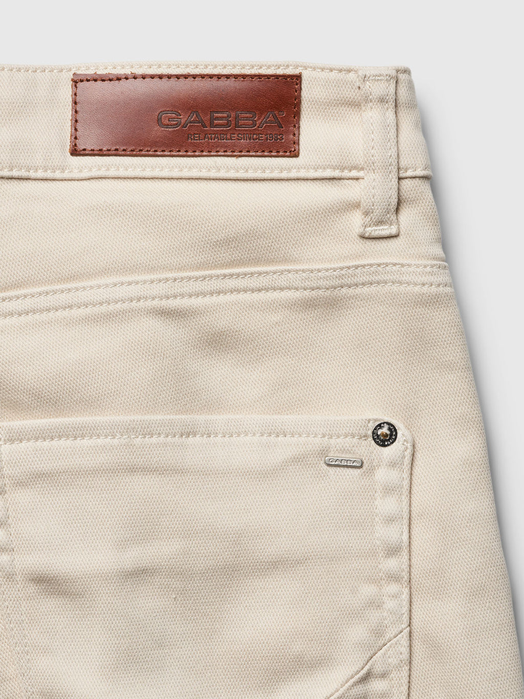 Close-up of Gabbas Jason K3995 SANZA Shorts in Birch, highlighting the back pocket with a brown leather patch embossed on the waistband. Reinforced pockets and metal rivets near the pocket enhance durability while textured fabric blends style with resilience.