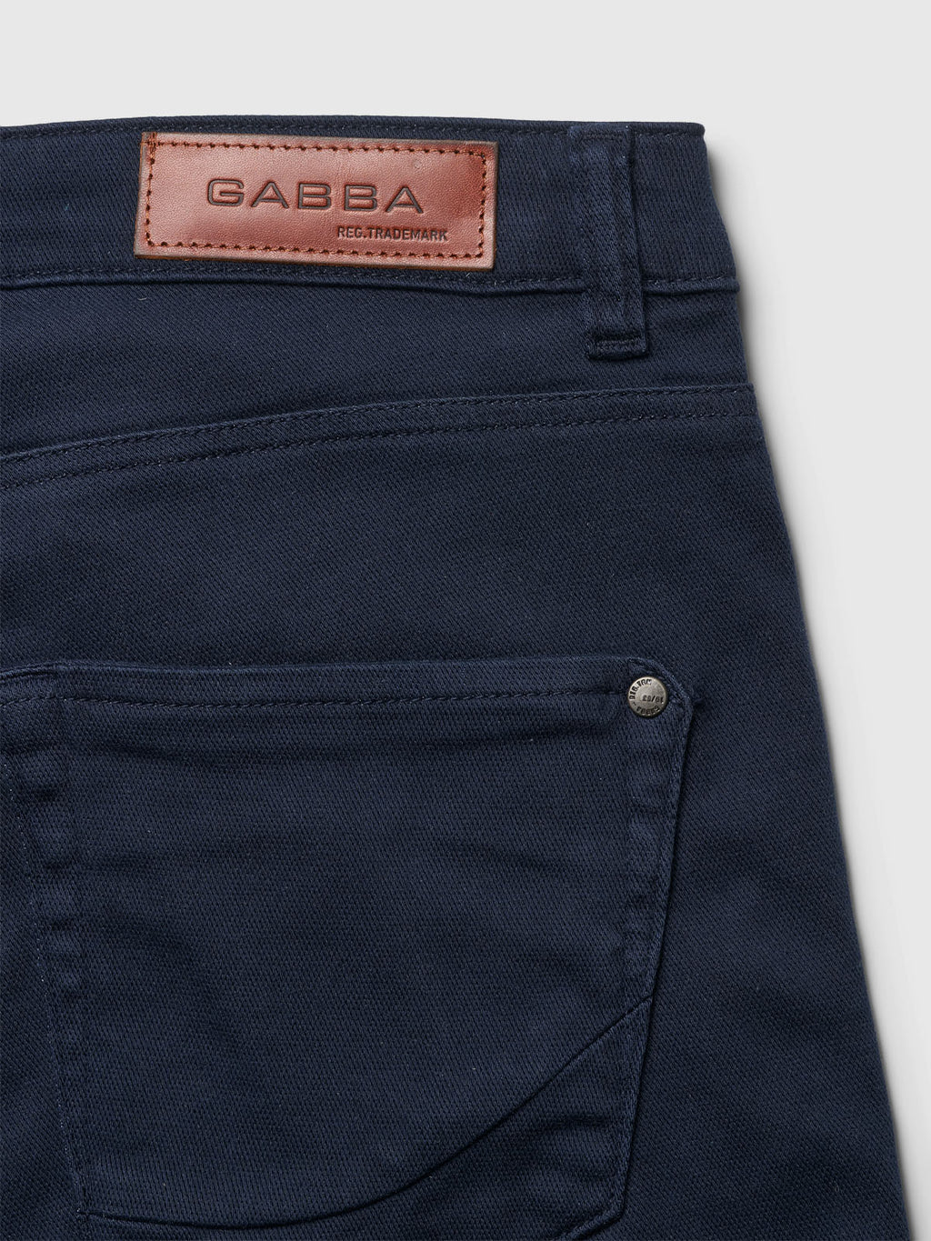 Close-up of navy Jason K3995 SANZA Shorts by Gabba, highlighting a back pocket with silver rivet and brown leather patch on the waistband. The super-stretch fabric beautifully showcases texture and stitching against a light background.