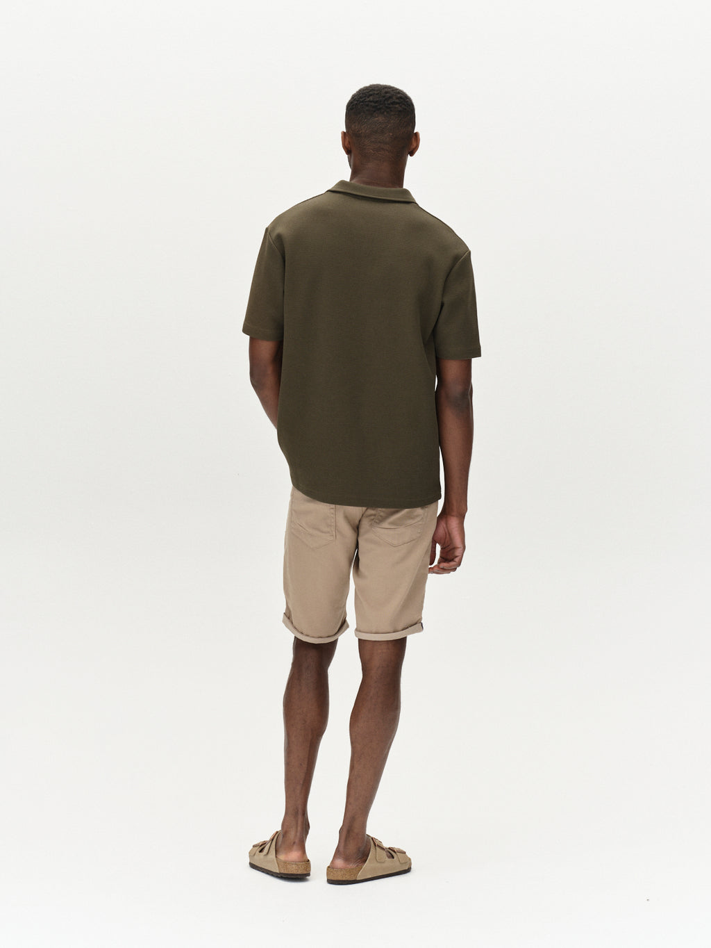 A man stands facing away, wearing a dark green short-sleeve shirt and Gabbas Jason K3995 SANZA shorts in Coriander. His sandals complete the look against a plain white background.