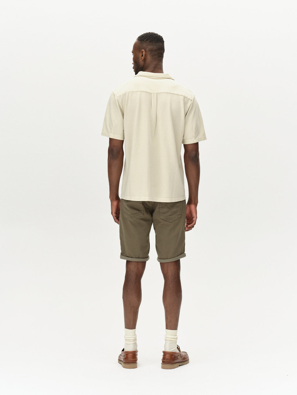 A person stands facing away, wearing a light short-sleeve shirt and Gabbas Jason K3995 SANZA Shorts in Dusty Olive. White socks peek out from their brown sandals, all set against a plain white background.