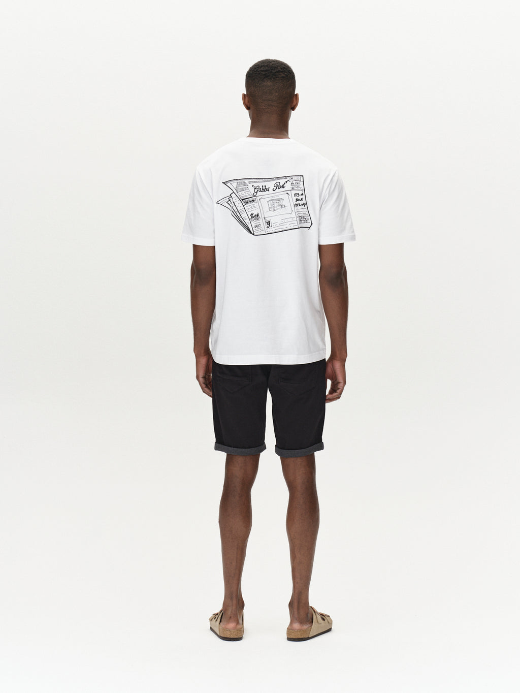 A person stands facing away, wearing a white T-shirt with two airplane tickets on the back. Paired with Gabbas Jason K3995 SANZA Knee-Length Black Shorts in super stretch fabric and sandals, the outfit exudes a relaxed vibe perfect for spring and summer against a plain white background.