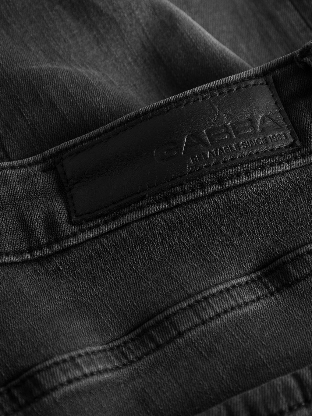 Close-up of a black leather label on charcoal fabric, embossed with Gabba, stitched onto Jones K3459 - Grey Denim, ensuring enhanced textures and stitching for the perfect fit.