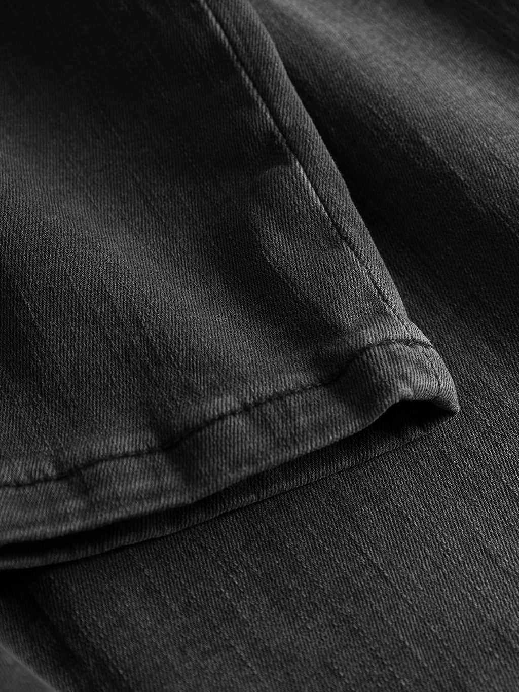 Close-up of the Gabba Jones K3459 - Grey Denim shows a neatly folded super-stretch fabric with visible texture, appearing smooth and slightly shiny in light. It promises a perfect fit with clean edges and subtle stitching along its hems.