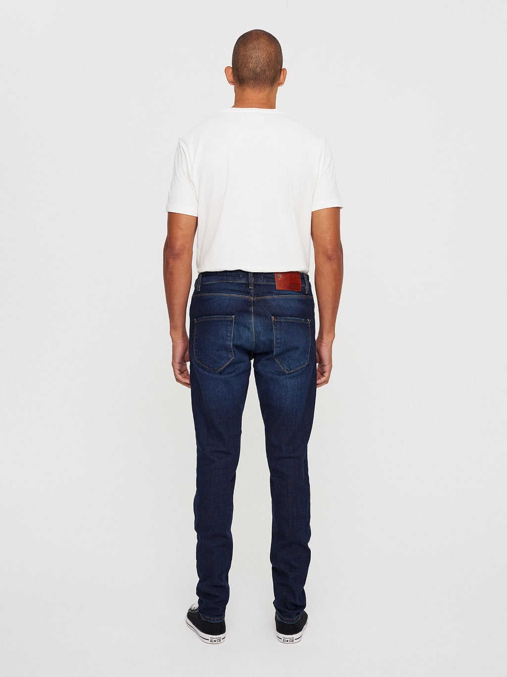 A person faces away from the camera, wearing a white t-shirt and Gabbas Rey K4441 - Mid Blue Denim jeans with black sneakers featuring white soles against a plain white backdrop.