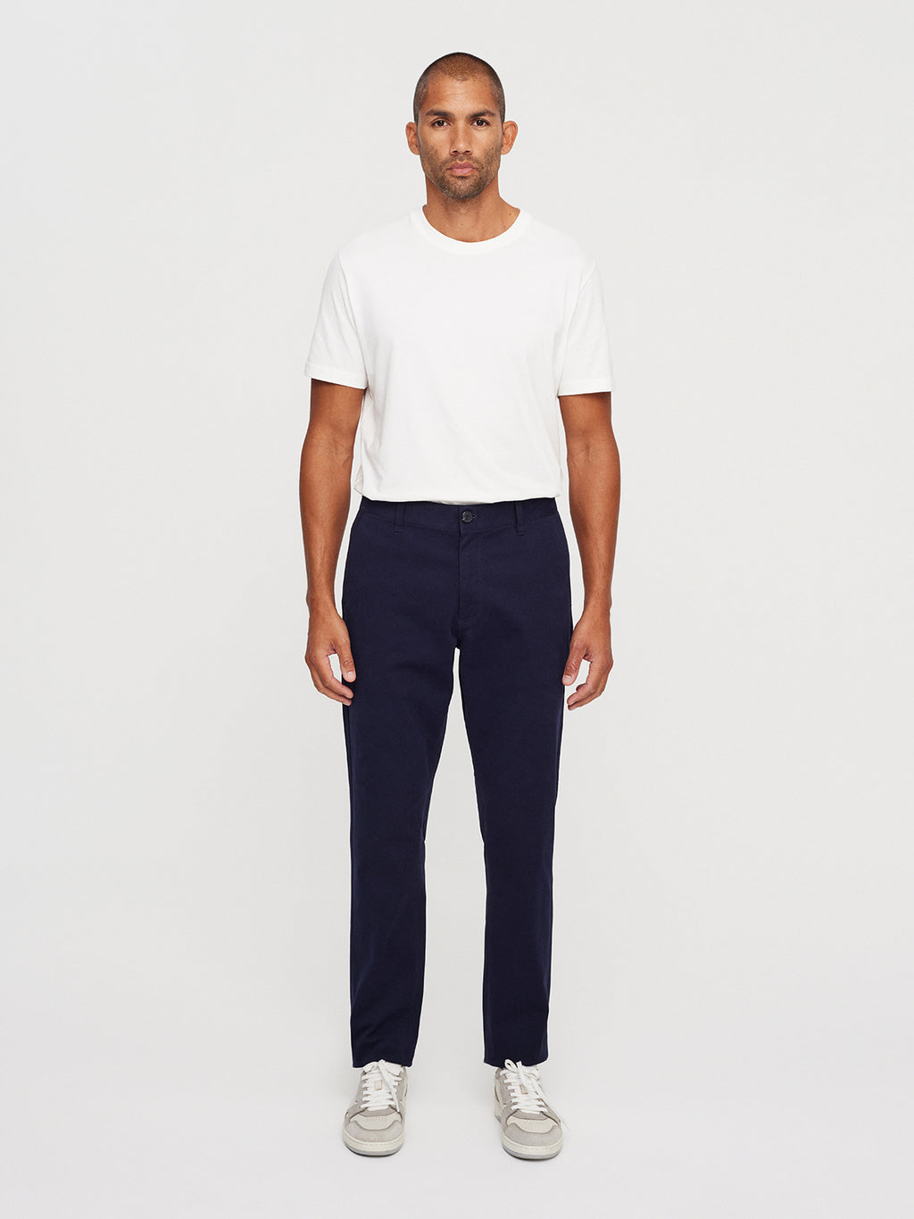 A person stands against a plain background wearing a classic look: a white t-shirt, Gabbas Venza Chino in Navy, and white sneakers.