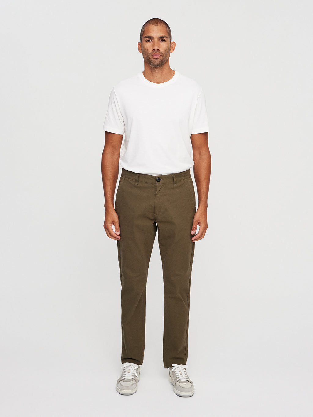 A person faces the camera, wearing a plain white T-shirt and Gabbas Venza Chino in olive green from the mens collection, paired with light sneakers. The neutral background highlights the regular fit of this outfit.