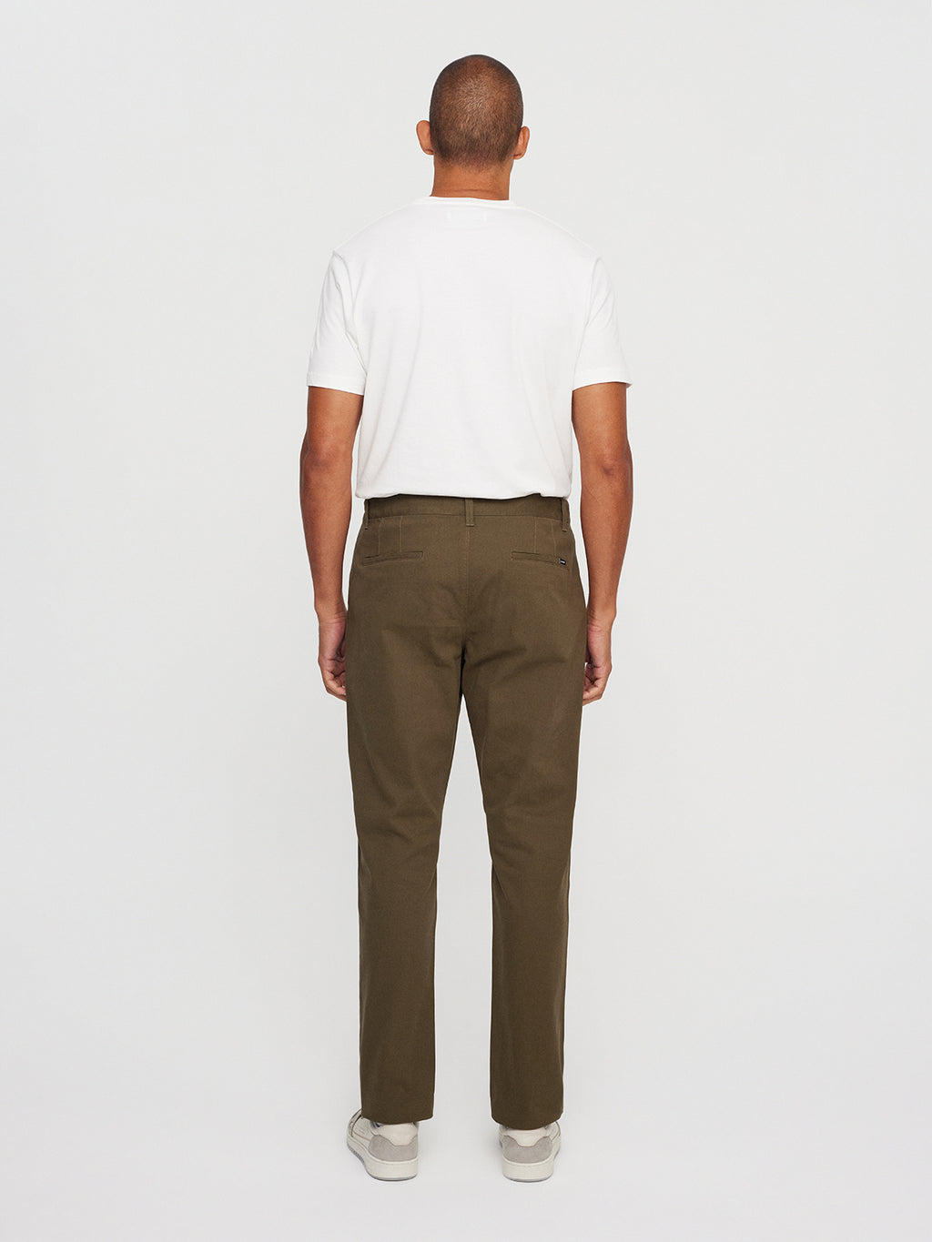 Facing away, a short-haired person dons Gabbas Venza Chino in olive green with a white T-shirt and light sneakers against a plain white backdrop, highlighting this wardrobe essential.