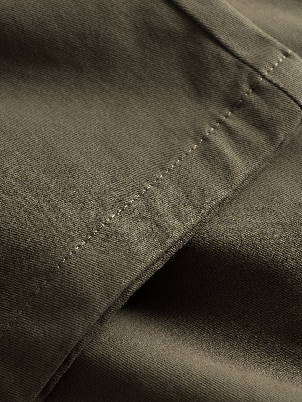 Close-up of Gabbas Venza Chino fabric in olive green, showcasing visible stitching and smooth, slightly folded texture, reminiscent of a timeless mens wardrobe staple.