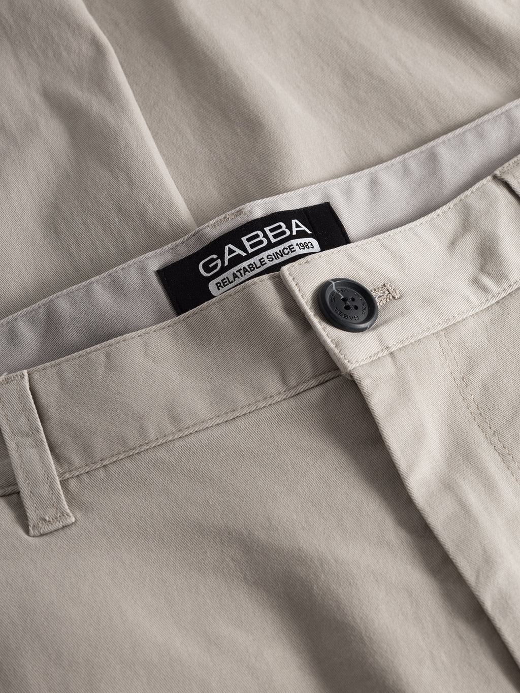 Close-up of Venza Chino - Lt. Sand with a tag reading Gabba Relatable Since 1983. These regular fit chino pants feature a buttoned closure and belt loops, making them a simple and classic staple for any mens wardrobe.