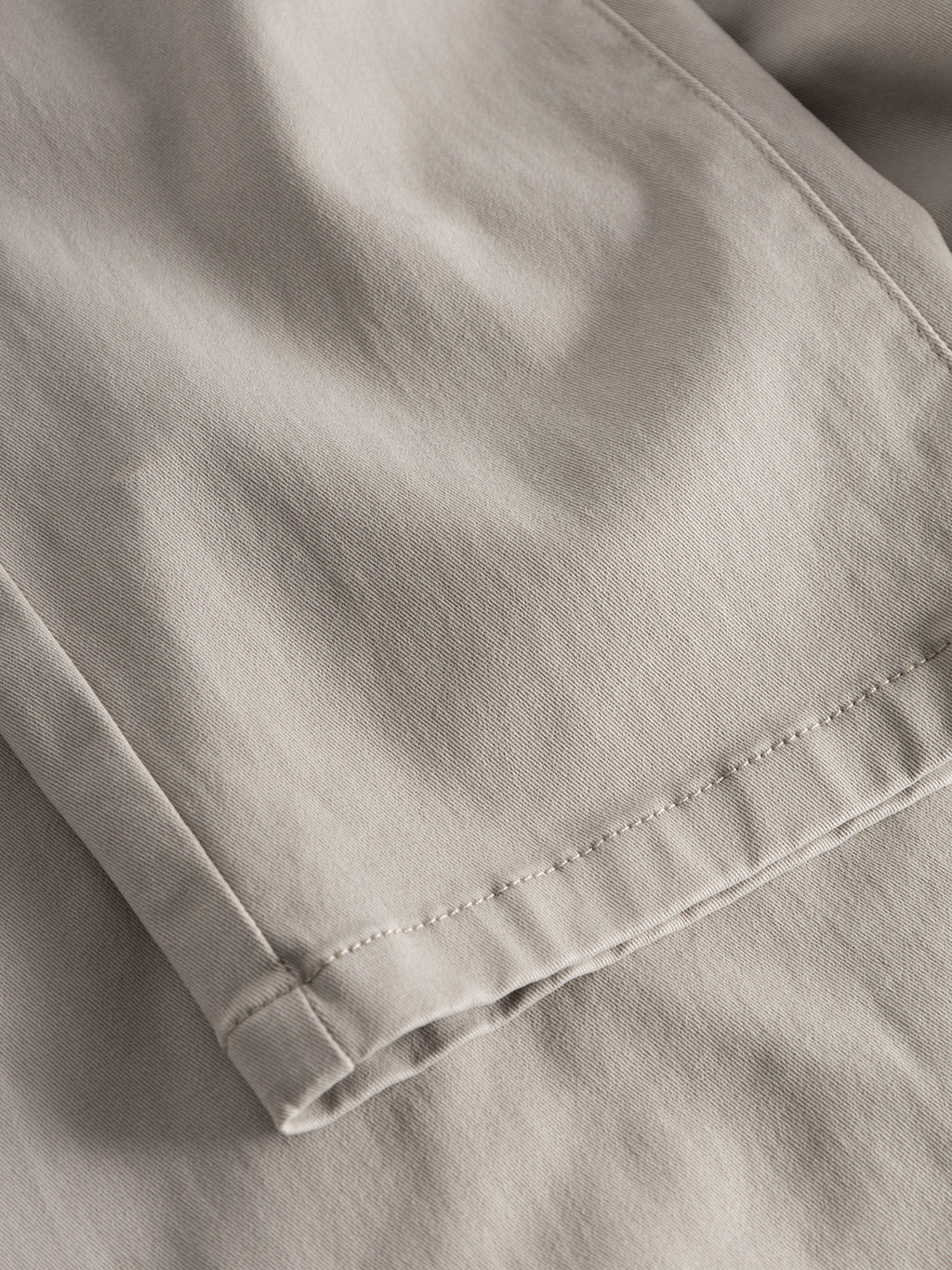 Close-up of folded Venza Chino - Lt. Sand fabric by Gabba, showcasing the texture and stitching along the edge. The smooth material with visible seam lines provides a minimalist and neutral look, perfect for any mens wardrobe seeking a regular fit.