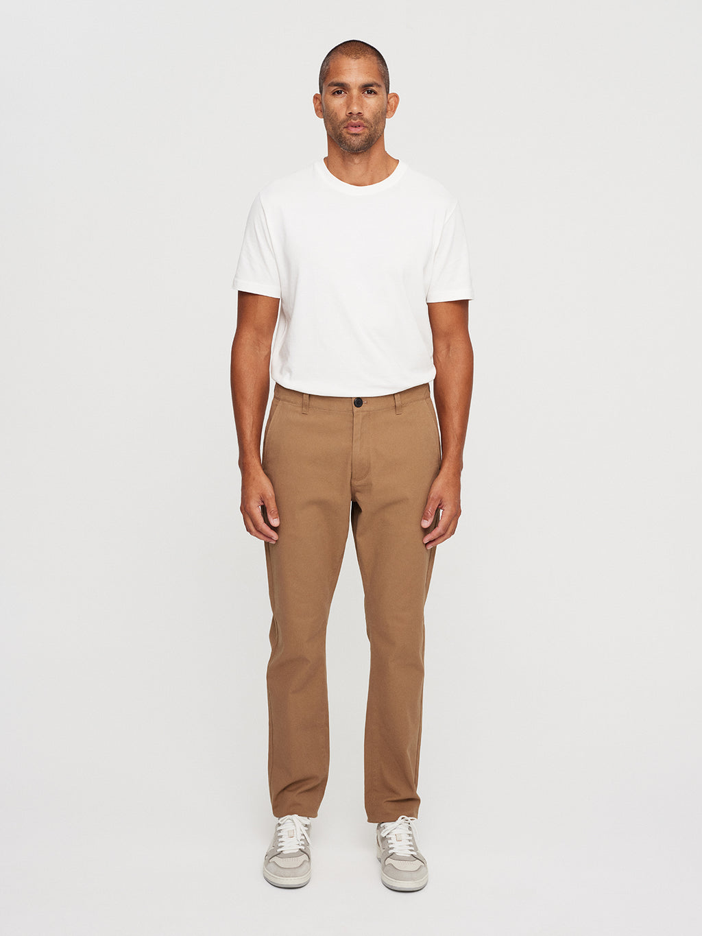 A man in a white t-shirt, wearing Gabbas Venza Chino in Light Brown and white sneakers, stands against a plain white background, showcasing essentials from the modern mens wardrobe.