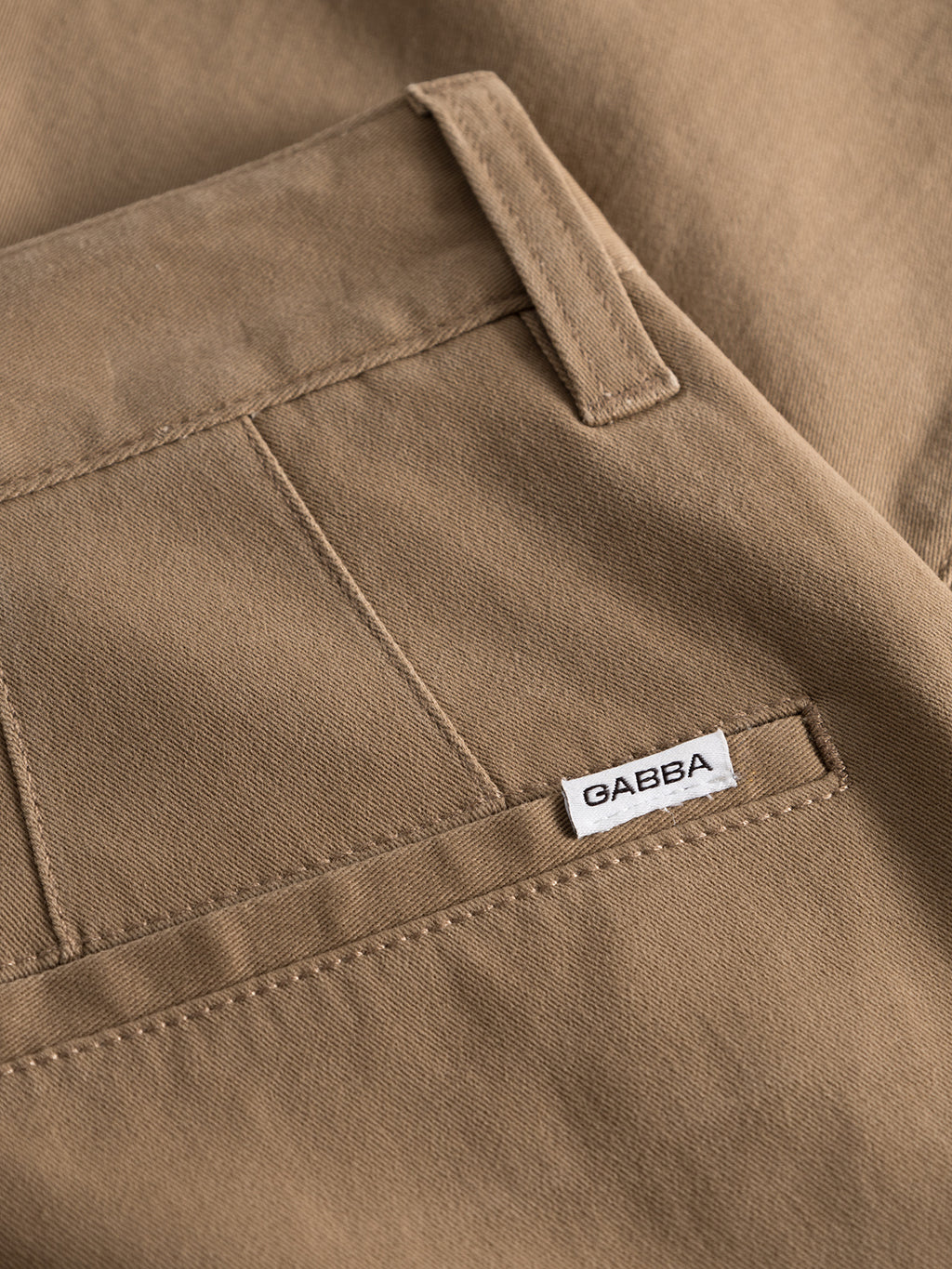 Close-up of Venza Chino - Lt. Brown pants, highlighting a back pocket with belt loops. A white Gabba label is sewn near the pocket. The smooth fabric and detailed stitching make these regular-fit chinos essential for any mans wardrobe.