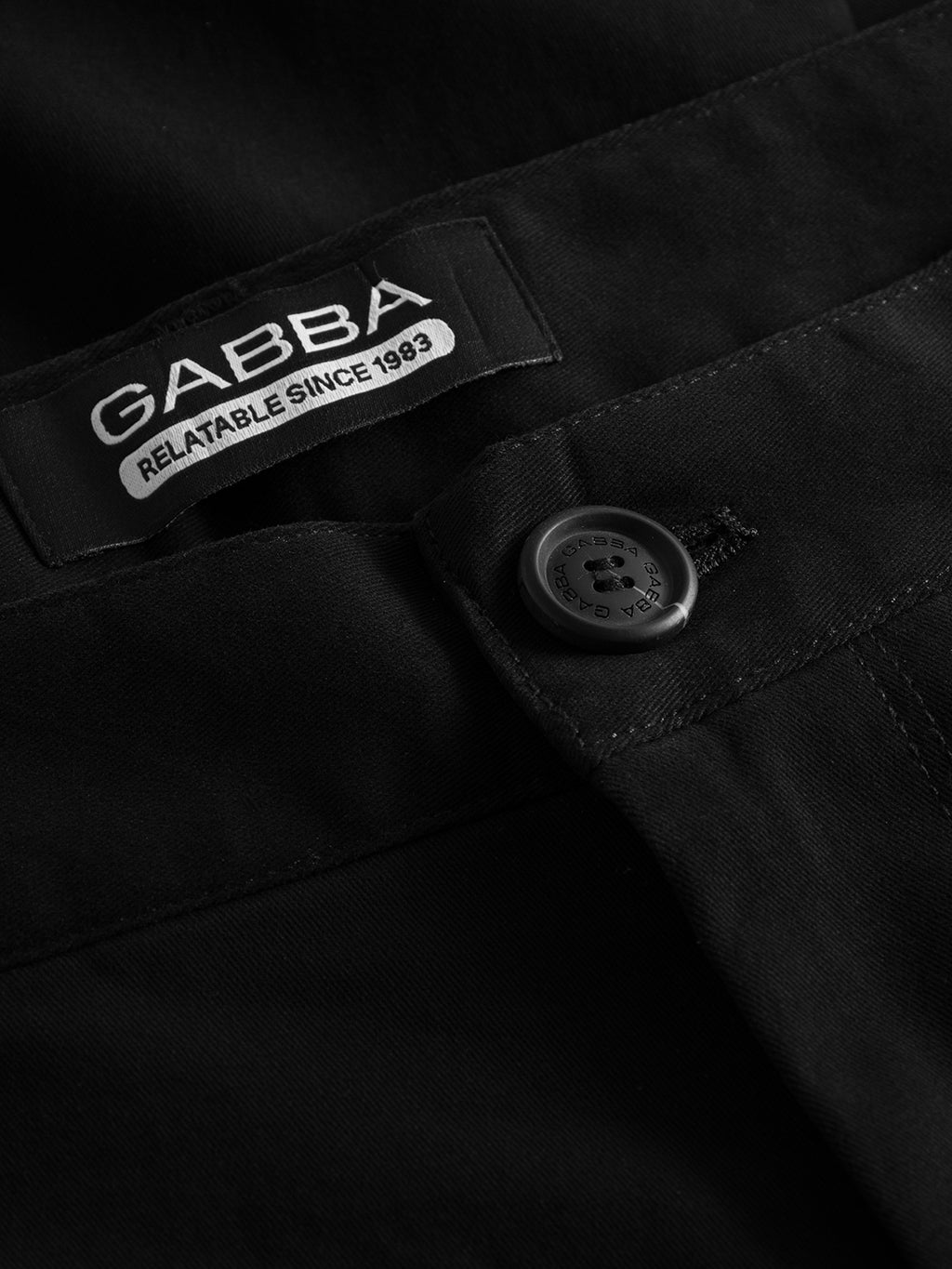 The Venza Chino in black by Gabba features a visible button and a waistband label reading Gabba, Relatable Since 1983. Essential for any mens wardrobe, it boasts smooth fabric and a classic regular fit.