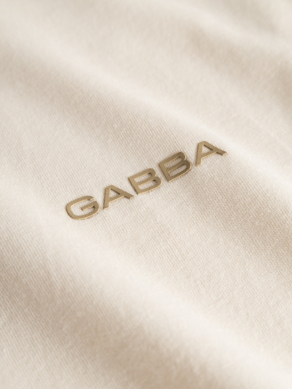 Close-up of the Gabba Dune Logo SS GOTS - Birch: soft GOTS-certified organic cotton in a cream tone, featuring “GABBA” embroidered in beige—an elevated twist on the classic tee.