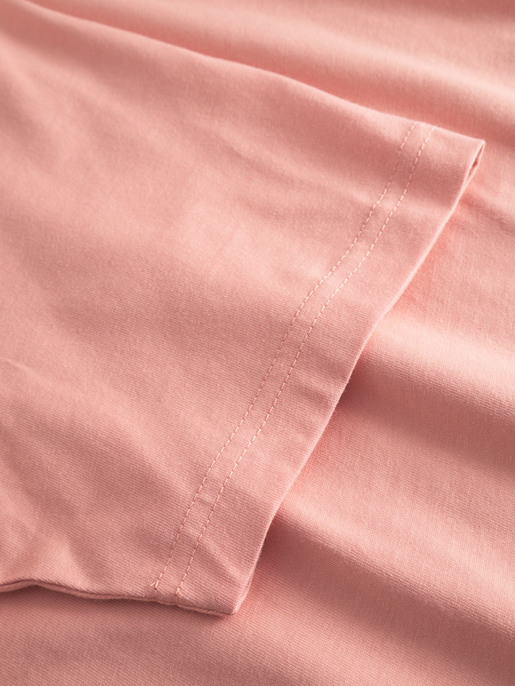 Close-up of folded Dune Logo SS GOTS - Rose Peach fabric from Gabba, with double-stitched seams. The soft, smooth texture hints at organic cotton, ideal for crafting a GOTS-certified basic t-shirt.