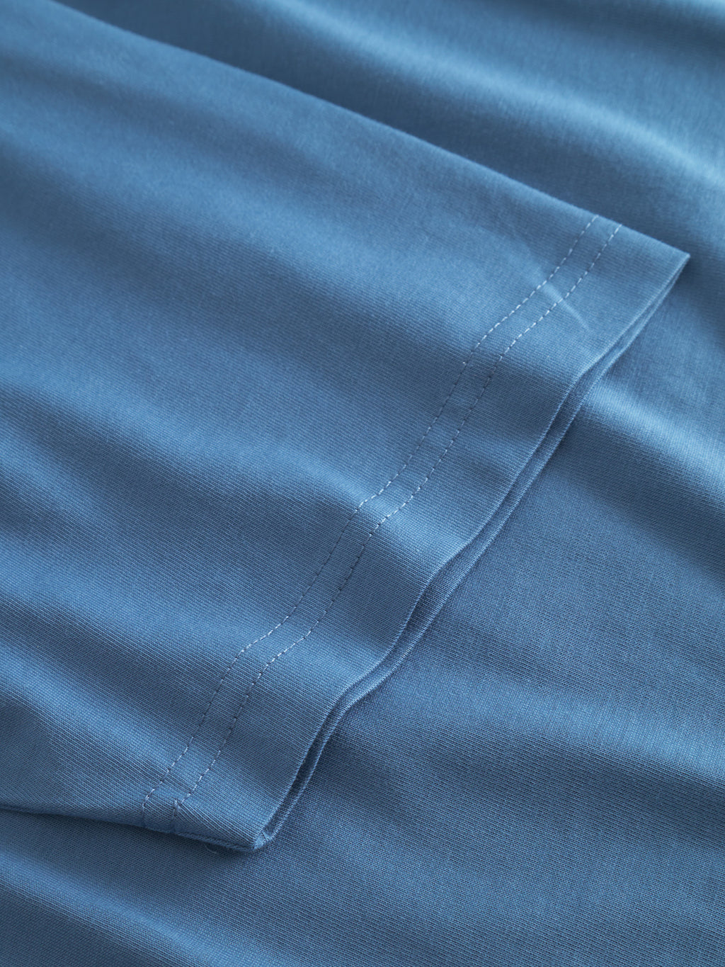 Close-up of the sleeve and hem of Gabbas Dune Logo SS GOTS - Blue Horizon t-shirt, highlighting its organic cotton fabric texture and double-stitched seams on a flat surface.