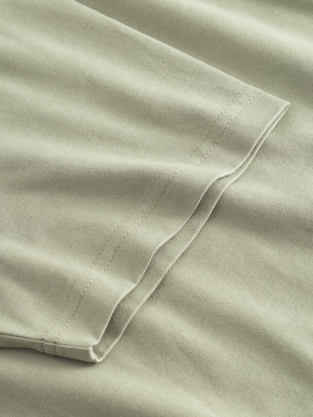 A close-up of the Gabba Dune Logo SS GOTS in light green shows a neatly stitched edge with visible lines. The smooth, lightweight texture suggests organic cotton, making it ideal for a comfortable basic T-shirt or pillowcase.