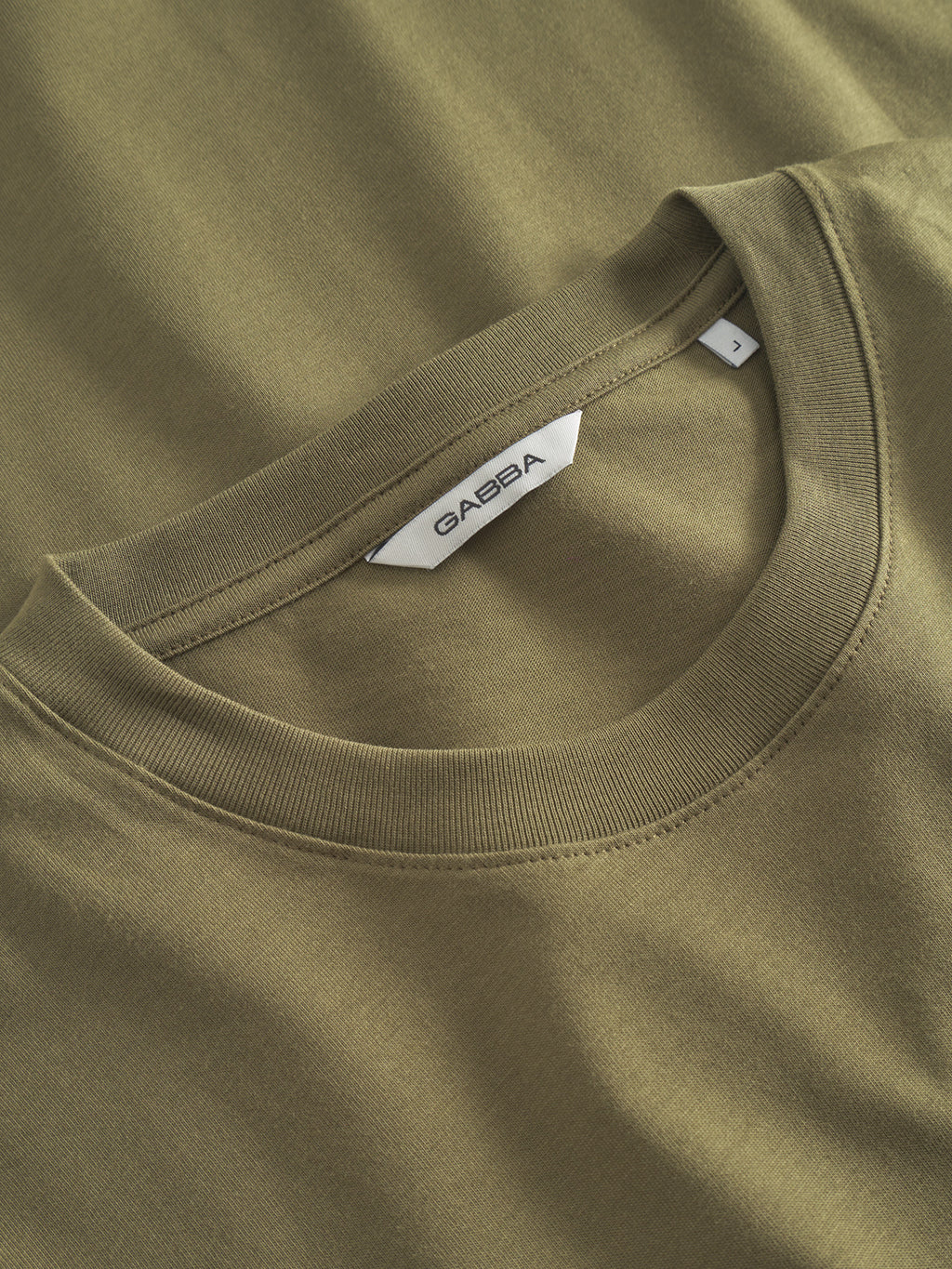 Close-up of an olive green crew-neck t-shirt, highlighting the neckline and Gabba tag. The Dune Logo SS GOTS shirt, made from GOTS-certified organic cotton, showcases smooth and soft fabric.