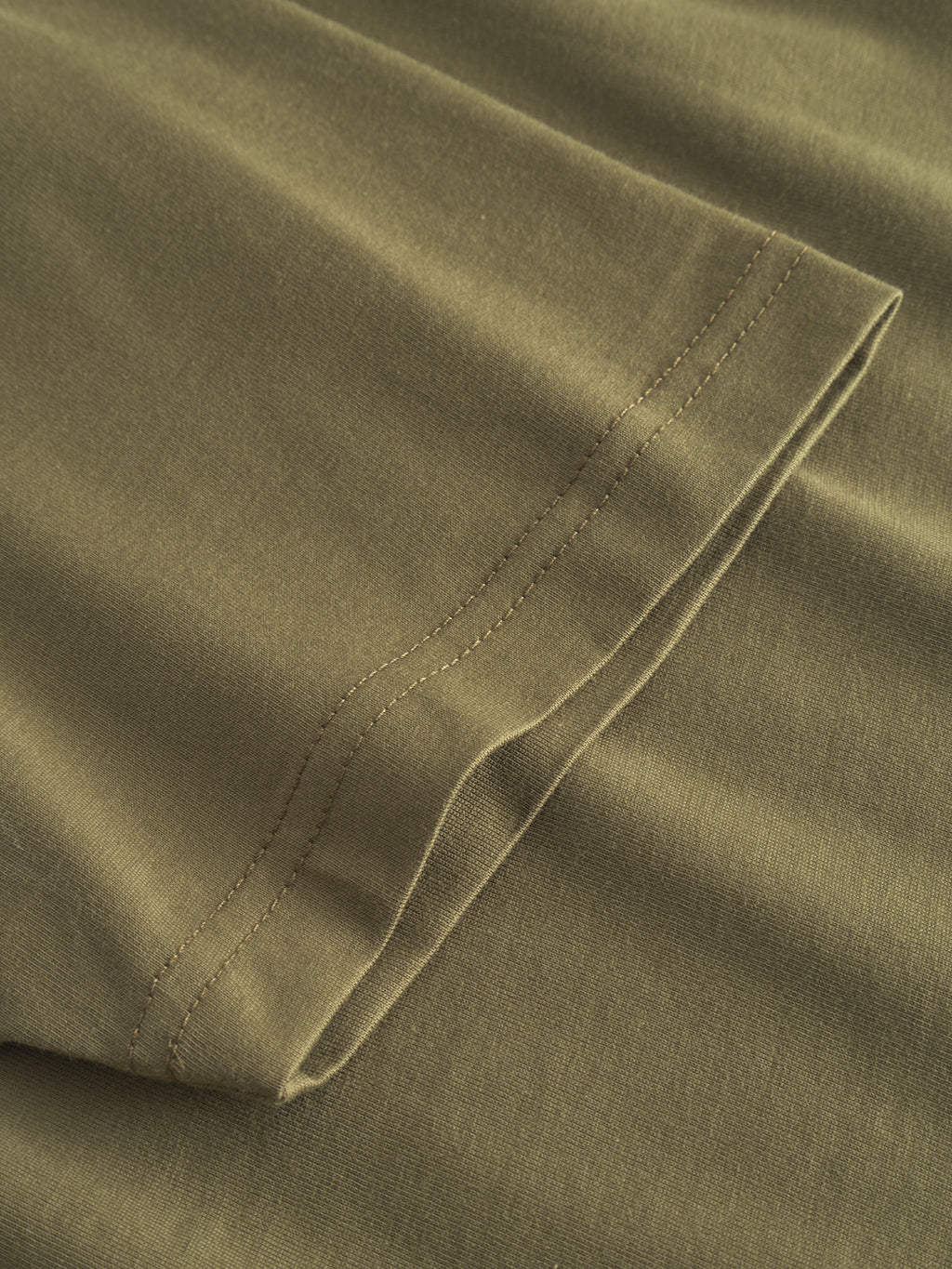 A close-up of the Dune Logo SS GOTS by Gabba reveals a neatly folded olive green sleeve with detailed stitching. The organic cotton fabric looks soft and smooth, emphasizing the garments GOTS-certified craftsmanship.