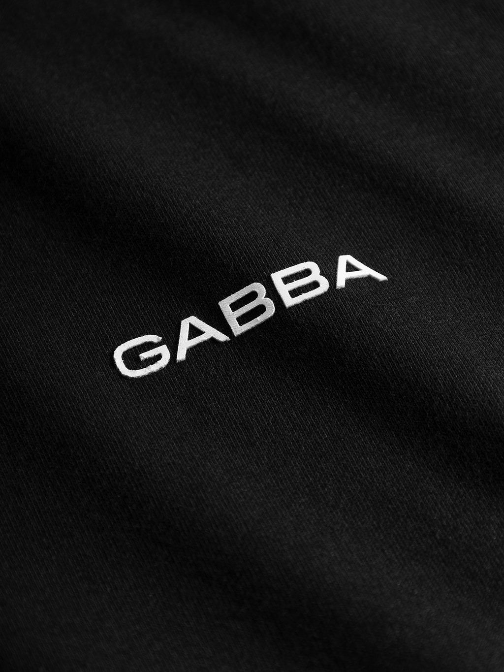 Close-up of black, GOTS-certified organic cotton fabric from the Gabba Dune Logo SS T-shirt, featuring GABBA embroidered in white uppercase letters at the center—ideal for a basic tee.