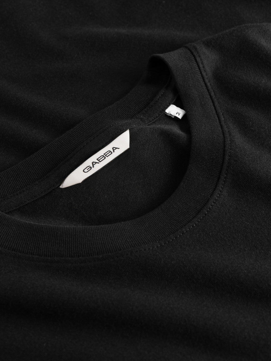 Close-up of the Gabba Dune Logo SS GOTS t-shirt in black, showcasing a white Gabba label and M size tag near the collar. Made from smooth, soft organic cotton for enhanced comfort.