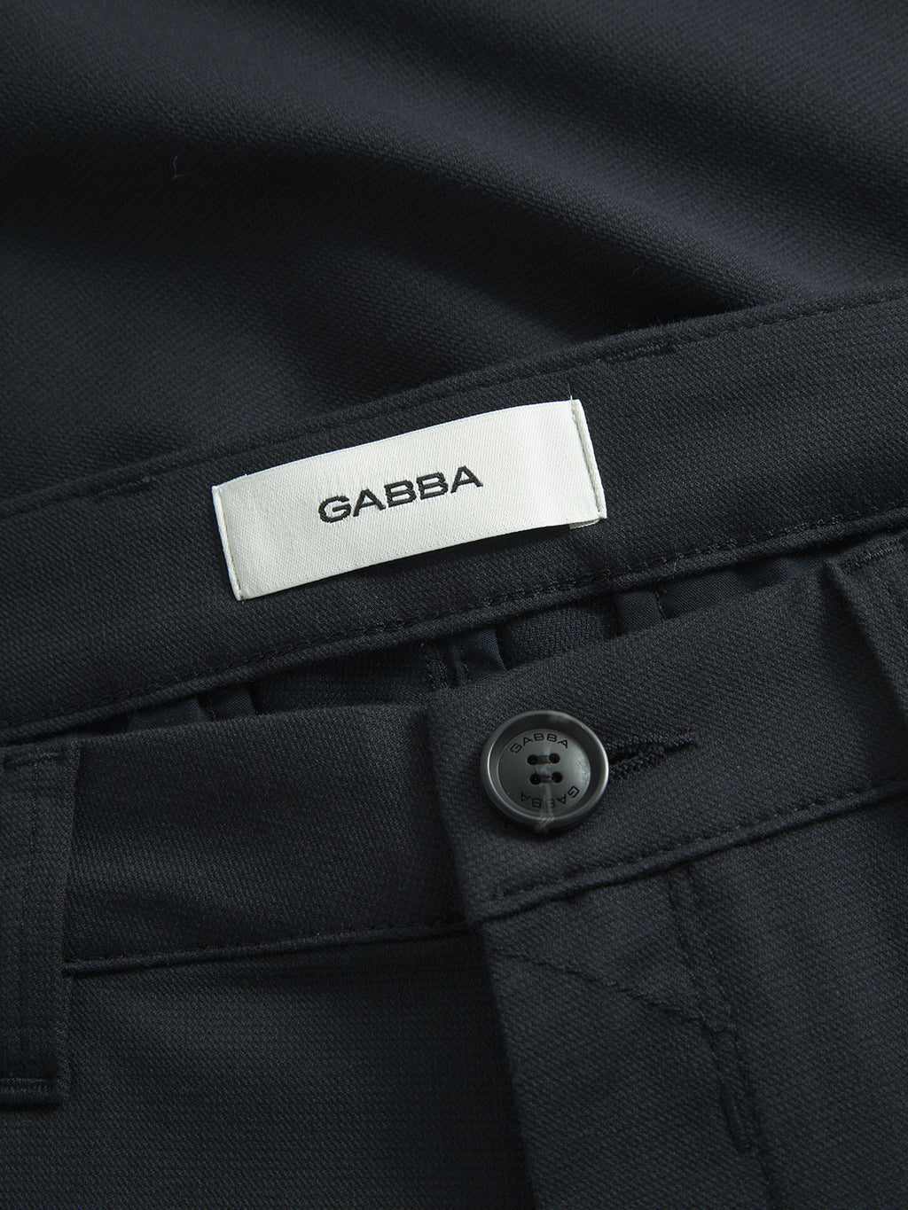 Close-up of sleek, formal navy pants by Gabba featuring a white label. The Paul Domo - Navy Mel chino pant offers elegance with its slim fit, button-secured waistband, and French pockets crafted from dark fabric.