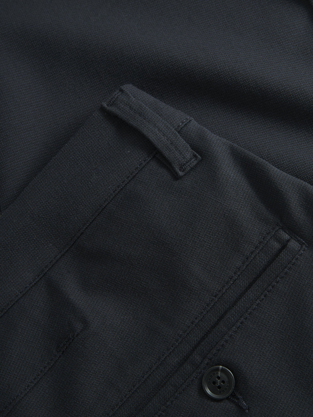 Close-up of Paul Domo - Navy Mel by Gabba, highlighting a textured dark fabric with a French pocket featuring a button fastener and flap. This slim chino pant displays meticulous stitching details around the branded buttons.