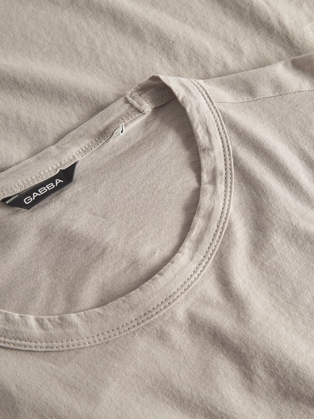 Close-up of a beige crew neck t-shirt with folded sleeve for all-day comfort. The tag inside is Gabba. Its soft, slightly textured fabric and classic fit make the Lagos SS - Sand a versatile wardrobe staple.