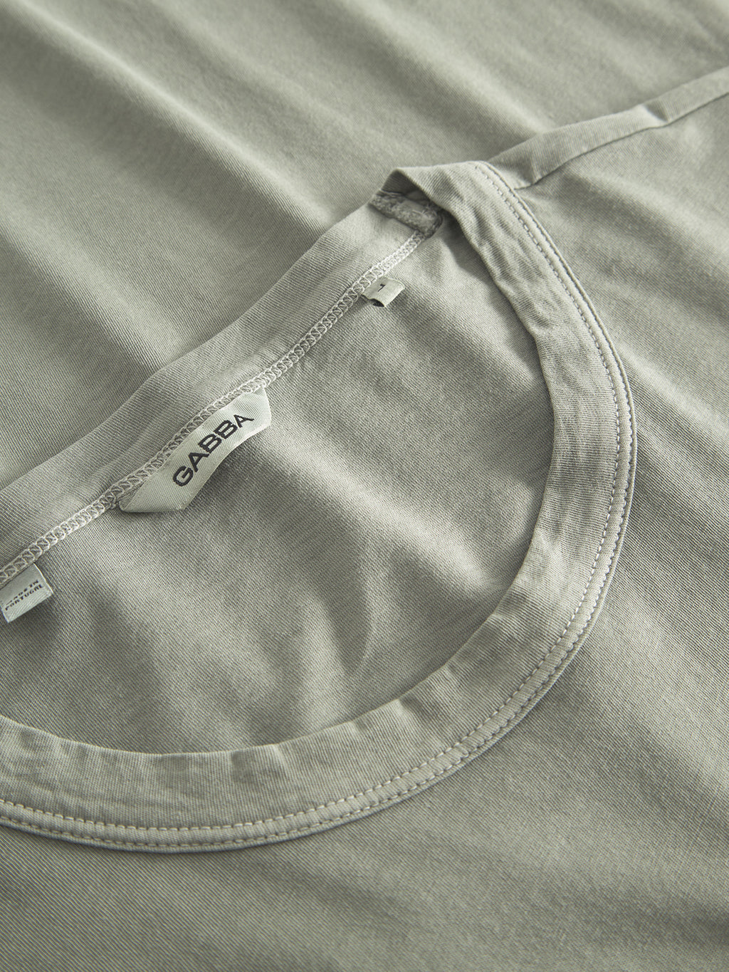 Flat lay of the Lagos SS - Green Sea T-shirt, featuring a comfortable round neckline and classic fit. The Gabba brand label is sewn into the collar, and the fabric looks soft and smooth, showcasing its simple yet elegant design.