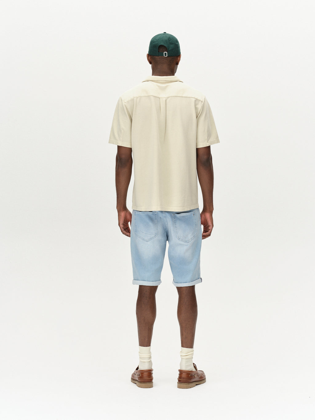 A person wearing a light beige short-sleeve shirt, Gabbas Markus K3987 Shorts in Lt. Blue Denim, brown sandals, and a green cap stands confidently against a plain white background.