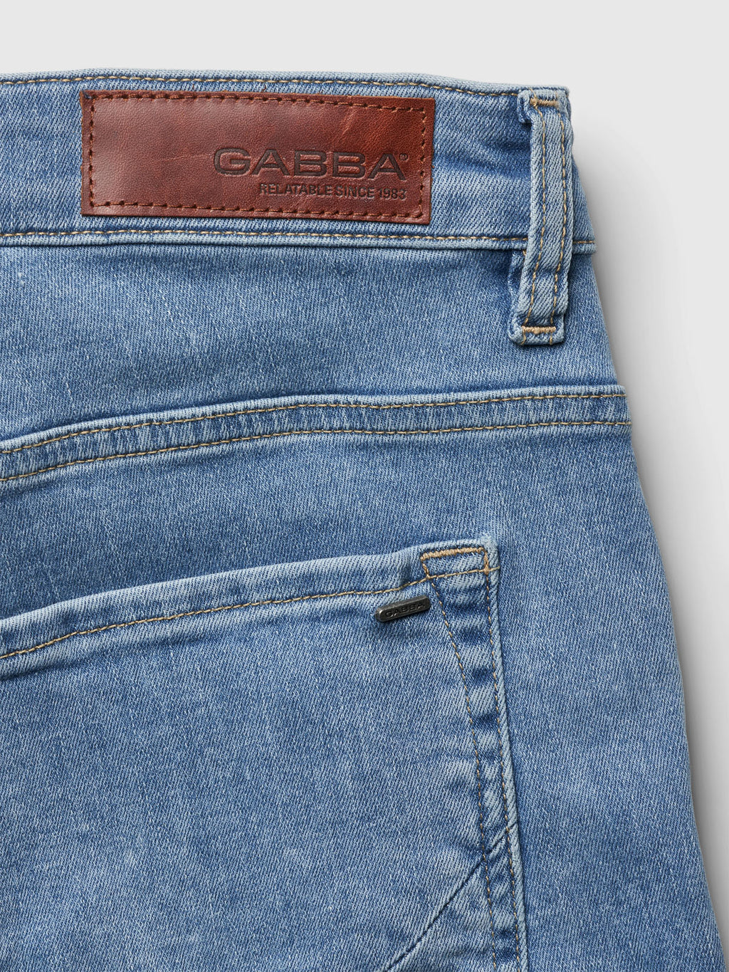Close-up of Markus K3987 Shorts in light blue denim with a brown leather patch by Gabba, stating Reliable Since 1983. The visible back pocket and stitching highlight a comfortable fit made from recycled viscose.