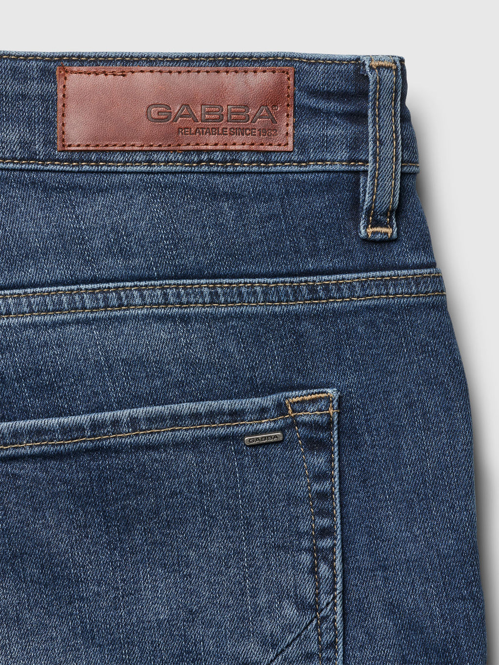Close-up of Markus K4664 Shorts in mid blue denim by Gabba, crafted from recycled viscose. They feature a brown leather waistband patch embossed with GABBA and RELATABLE SINCE 1983, offering comfort and a stylish back pocket with a small fabric tag displaying the brand name.