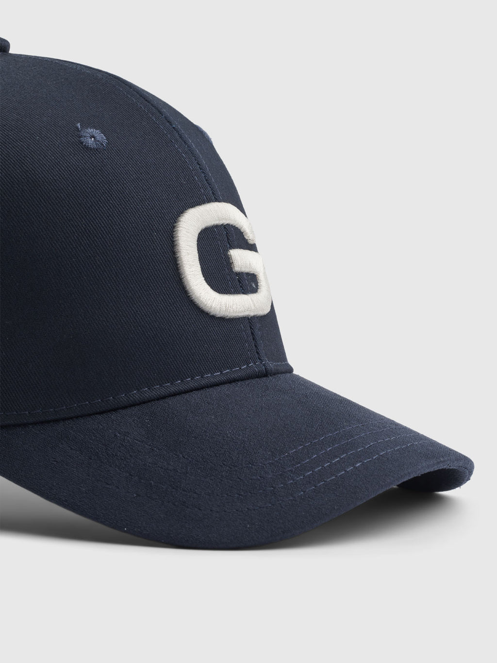 The Base - Navy cap by Gabba showcases a modern design with a large embroidered white G on the front. The image highlights its curved brim and classic fit against a light gray background.