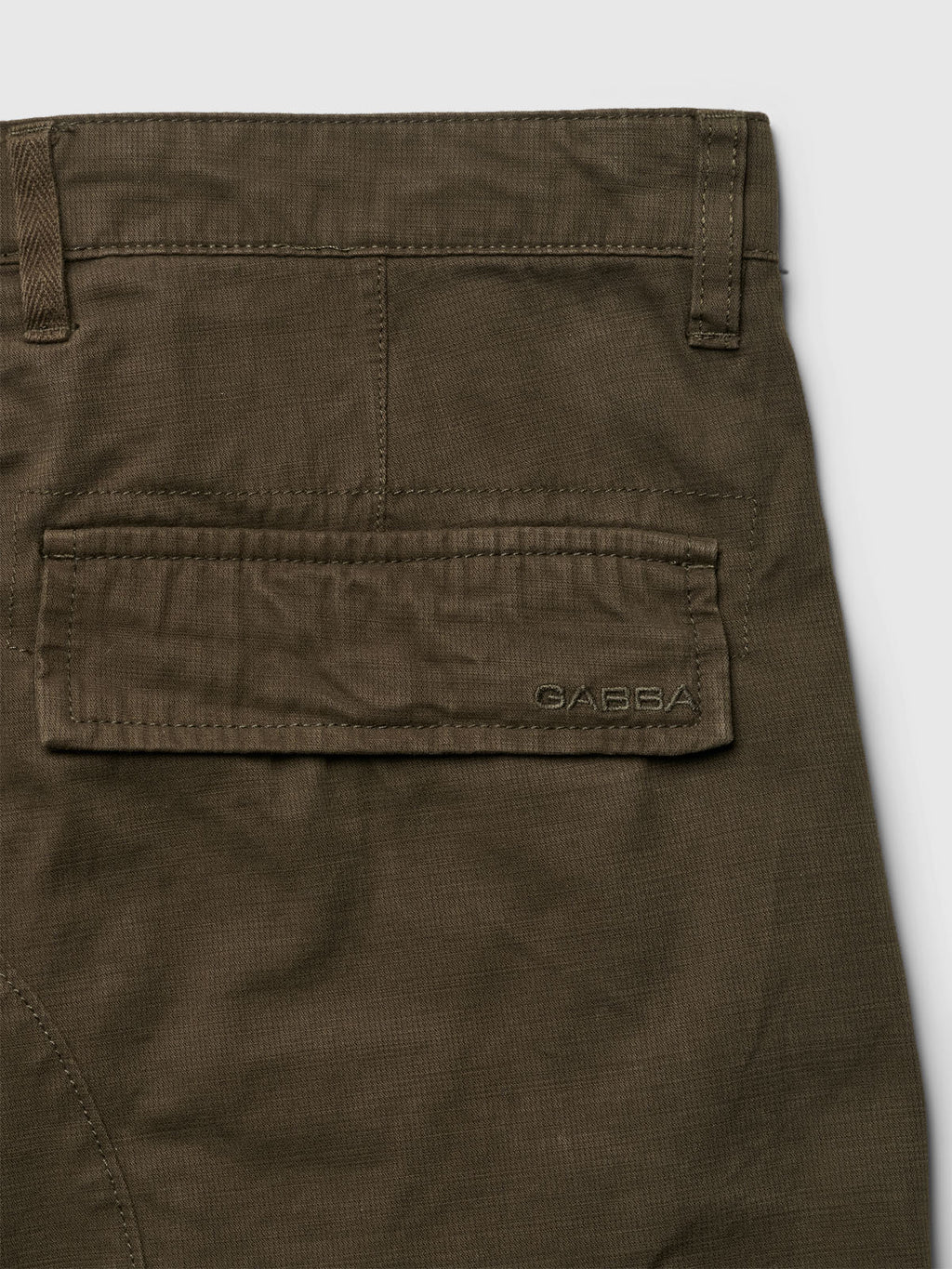 The Rodi Cargo Pant in Grape Leaf by Gabba showcases a close-up of olive green cargo pants with a flap pocket and belt loop; the brand name is embroidered near the pocket. Made from cotton, it features a subtle texture for added style.