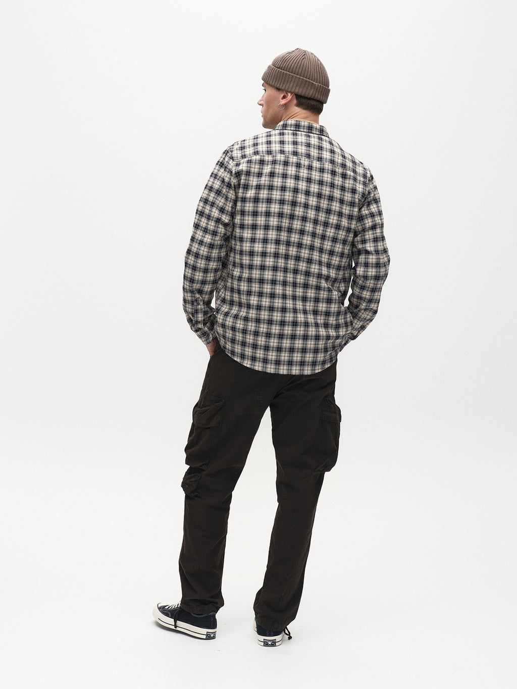 A person in a brown beanie, plaid shirt, and black sneakers stands with their back to the camera against a light backdrop, wearing Gabbas Rodi Cargo Pant in Black, featuring comfort stretch for ultimate ease and style.