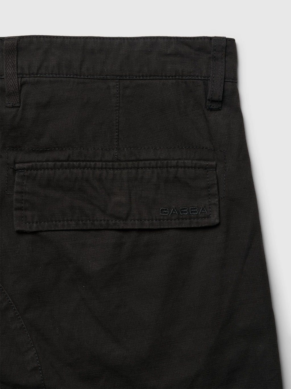 A close-up of the back pocket on Gabbas Rodi Cargo Pant in black highlights a flap with stitched logo, detailed stitching, and comfort stretch cotton fabric against a neutral gray background.