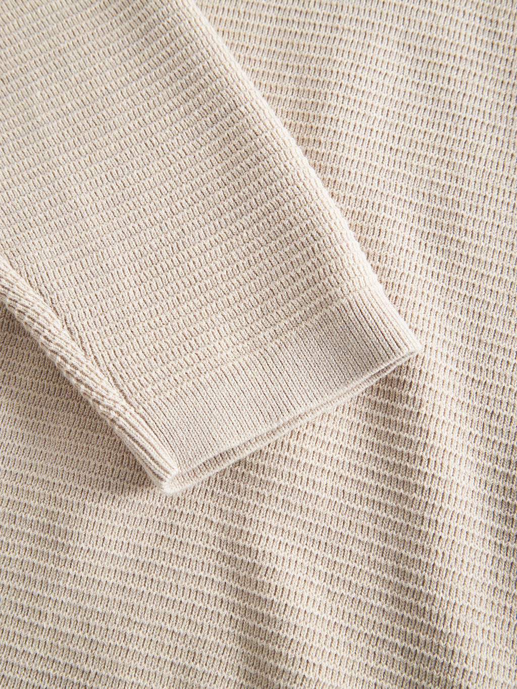 Close-up of the Lambo LS - Birch by Gabba, highlighting a long sleeve laid flat. Its cozy texture, created using classic knitting techniques, showcases a tightly woven pattern reminiscent of a traditional jumper.