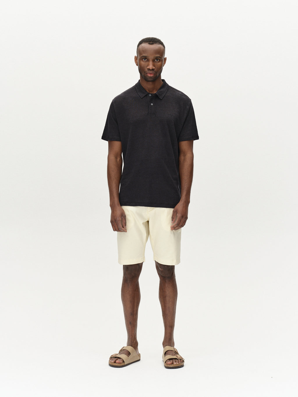 A person is shown against a plain background in a black polo shirt, Gabbas Jet K3280 Dale Shorts in Ecru Light, and brown sandals. They face the camera directly with arms at their sides, highlighting the outfits versatility.