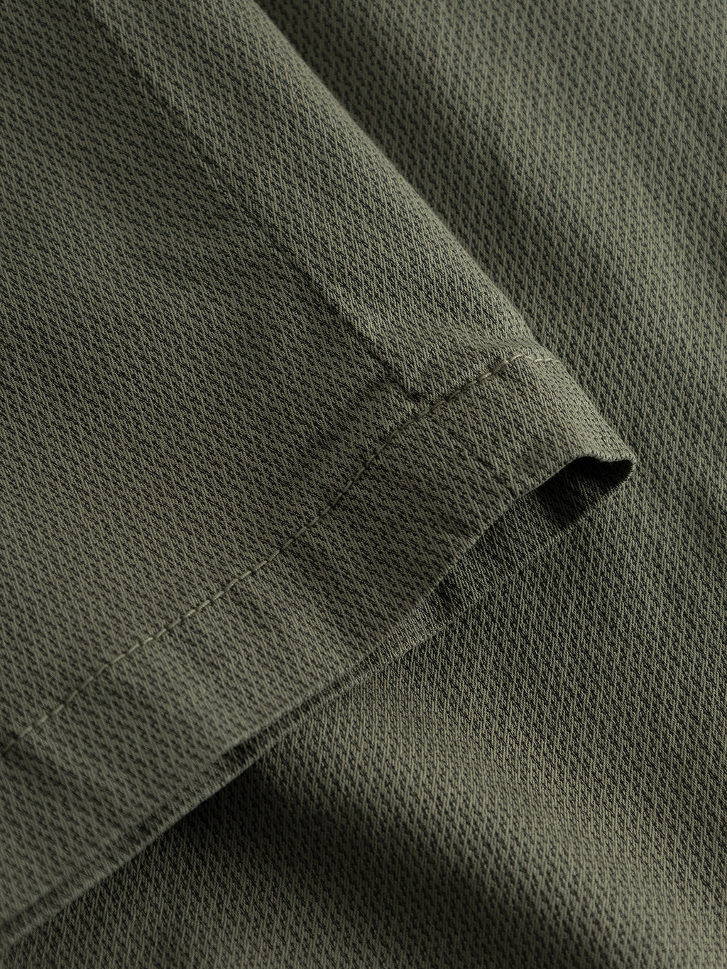 Close-up of the Gabba Jet K3280 Dale Shorts in Deep Lichen Green. The fabrics textured, waffle-like pattern catches the light, adding a subtle sheen and modern style. Neatly stitched along the edge, these shorts embody contemporary design.