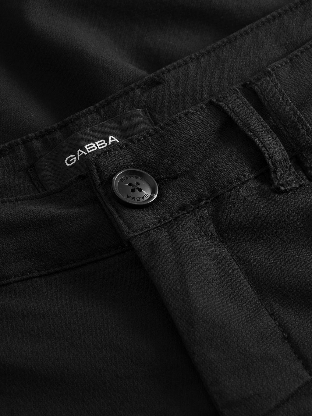 Close-up of Jet K3280 Dale Shorts - Black, highlighting a visible button with engraved text and belt loop. The interior features a dark fabric label with Gabba, showcasing the shorts modern design and texture for all-day comfort.